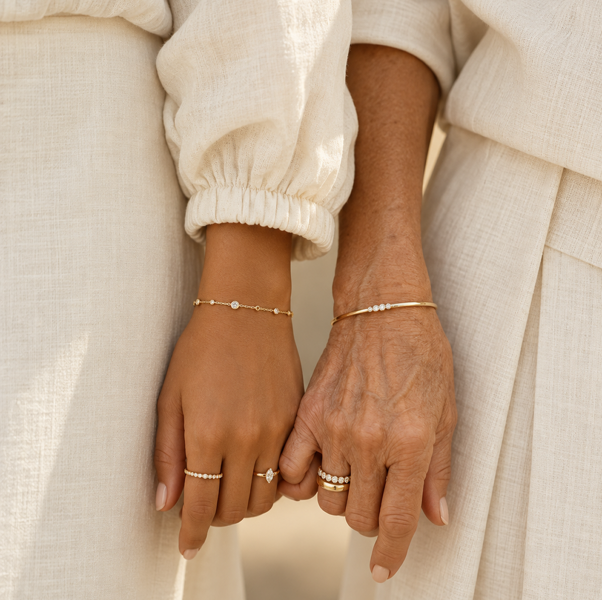 Close-up of two women from different generations standing side by side in ivory clothing, wearing delicate gold and diamond rings and bracelets, evoking continuity, memory, and jewelry passed through time.
