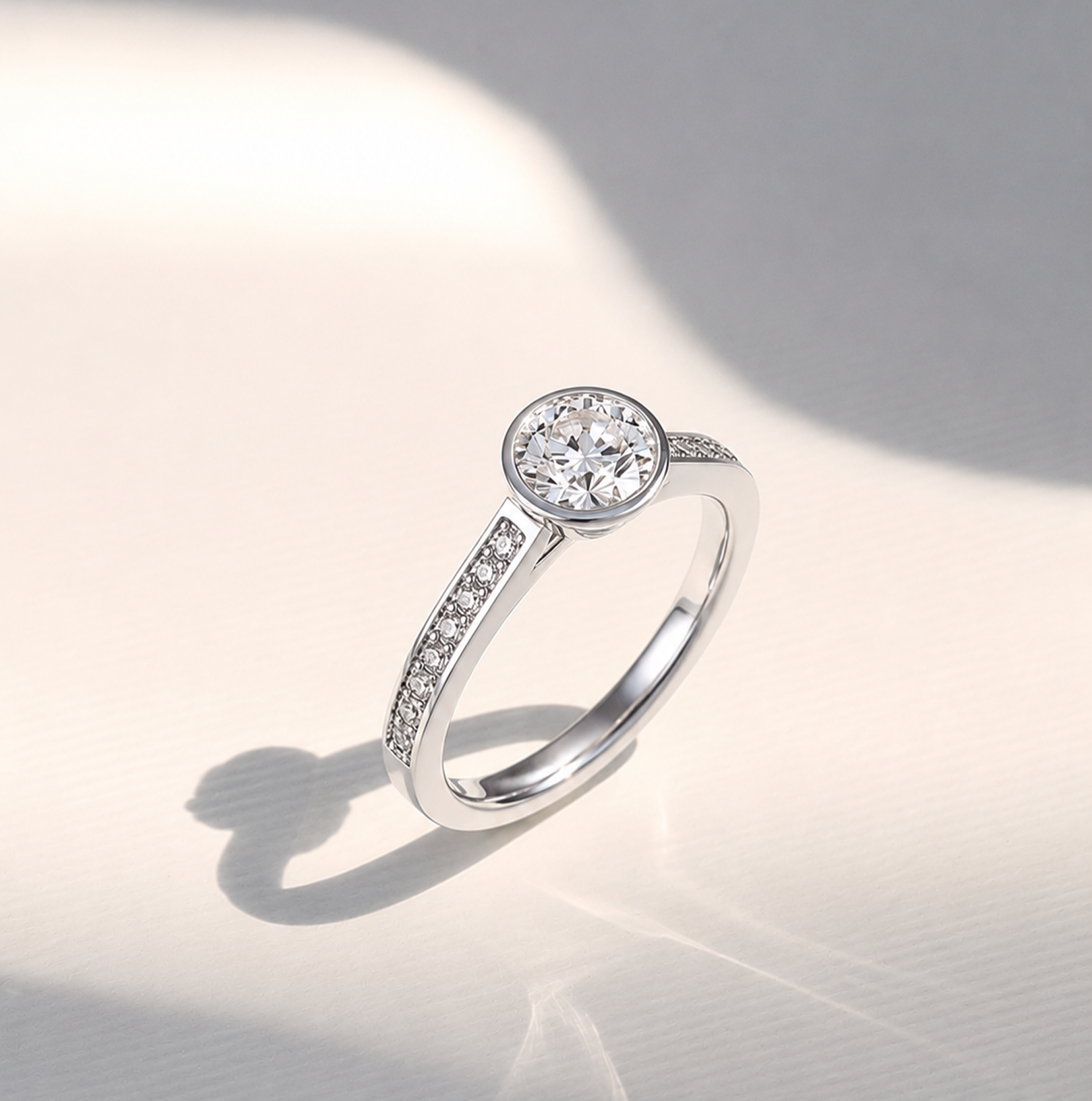 Matanee diamond engagement ring in white gold featuring a round brilliant-cut center diamond in a bezel setting with pavé-set diamond shoulders, photographed in soft natural light.