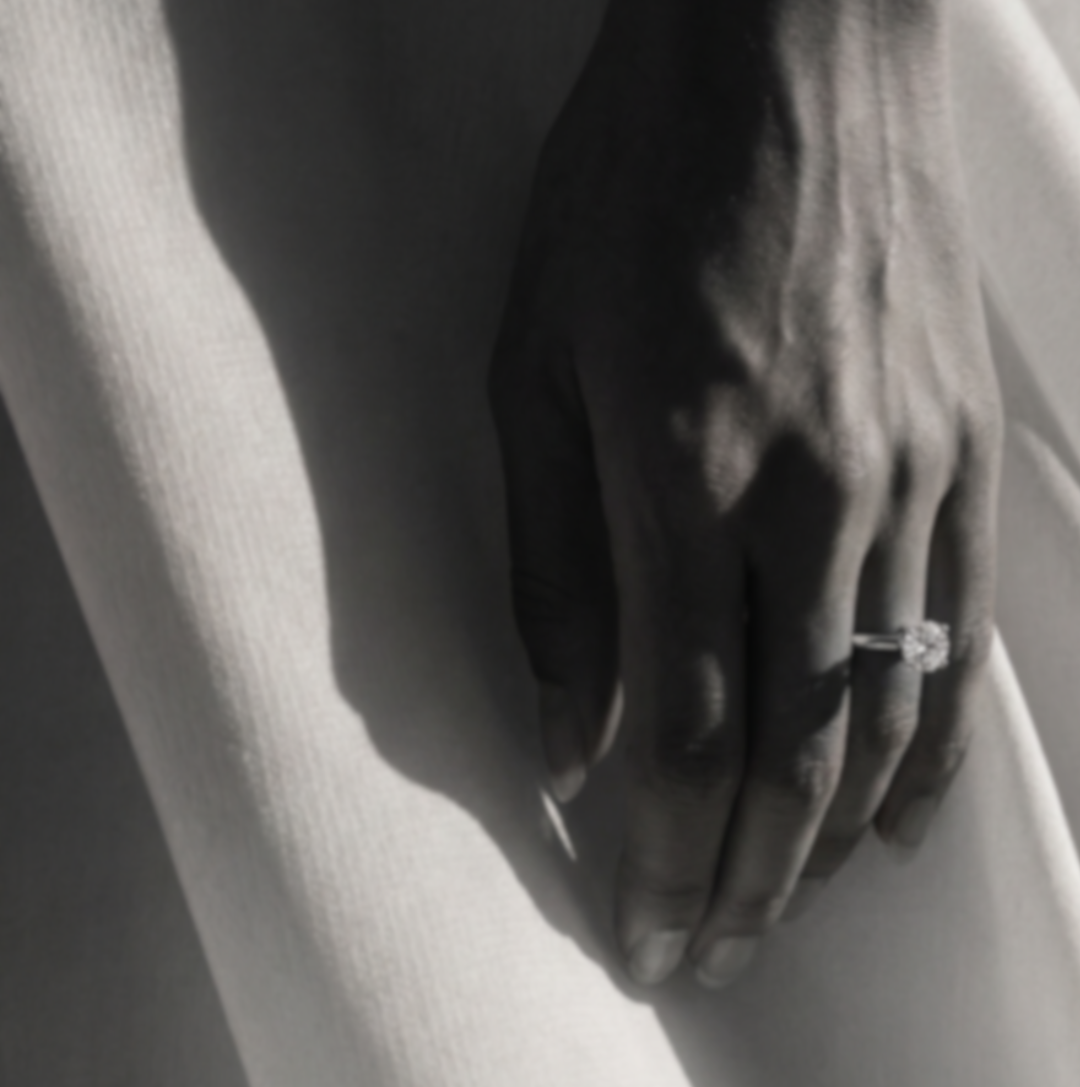 Close-up of a hand wearing a solitaire diamond ring against a softly draped white fabric.