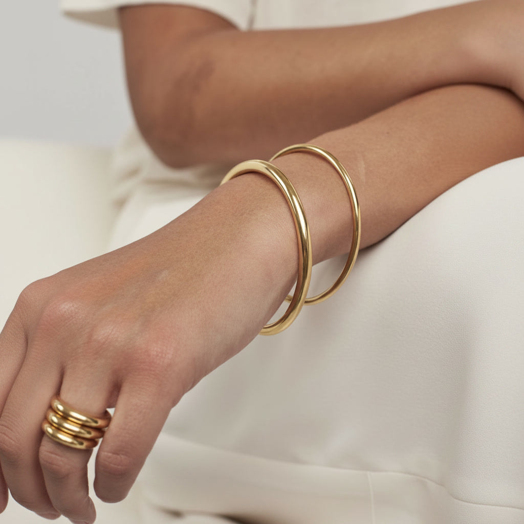 Classic Gold Bangle Bracelet: model wearing two gold bangles and stacked rings with an ivory outfit.