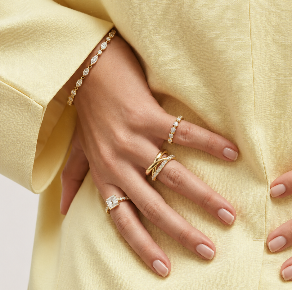 Close-up of a woman in a soft yellow suit wearing layered Matanee diamond and gold rings with a delicate diamond bracelet, styled in a refined fine-jewelry look.